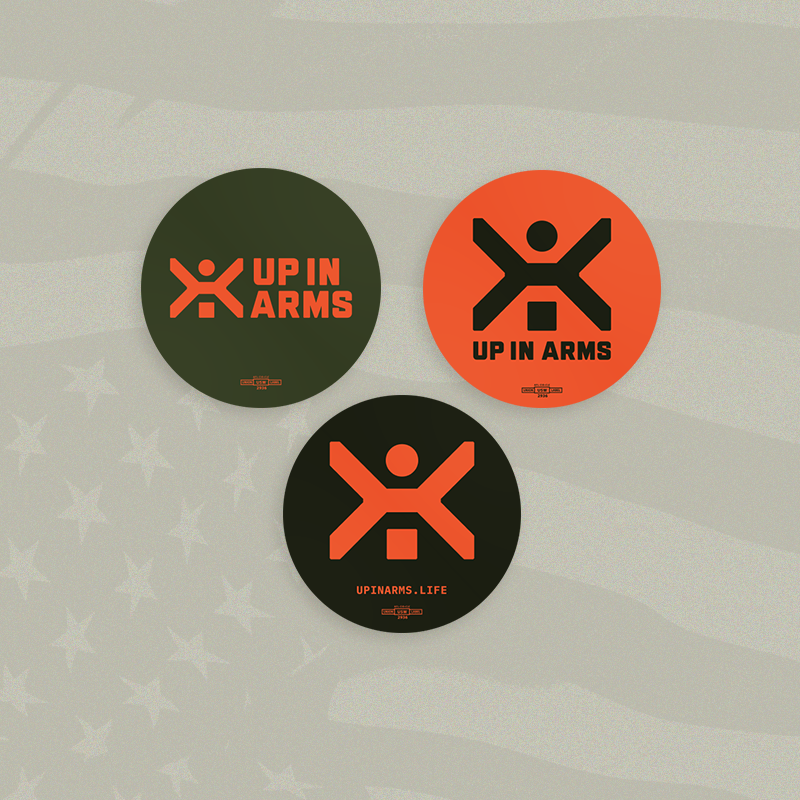 Three round stickers with 'Up in Arms' logo on a textured gray background